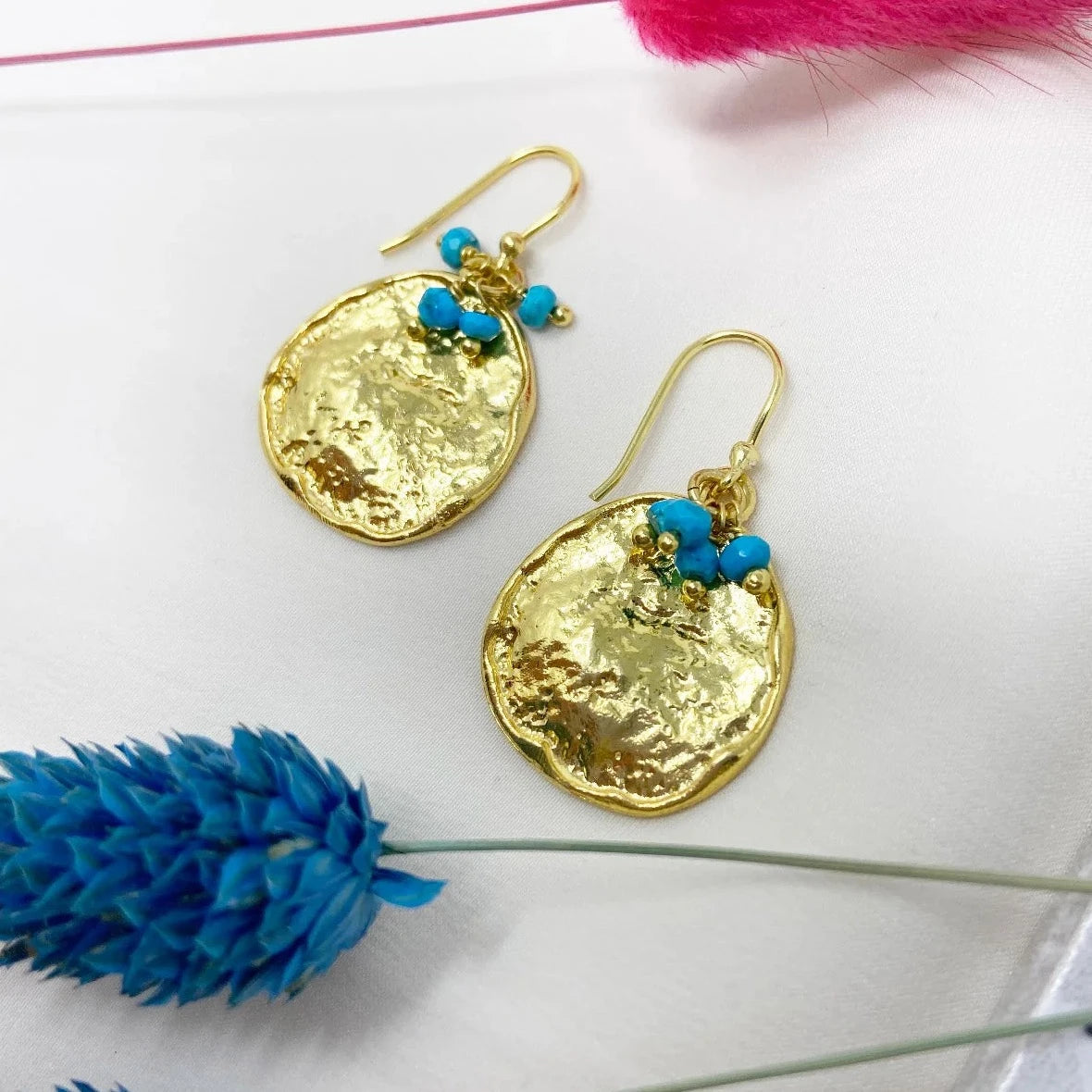 These handmade, drop earrings from Mazzi D Fiori, feature a rustic textured coin design and are adorned with turquoise gemstone beads and faceted semi-precious mini beads. Made with gold-plated materials, they are lightweight and versatile, perfect for both everyday use and more formal events. This style is a timeless addition to any accessory collection.